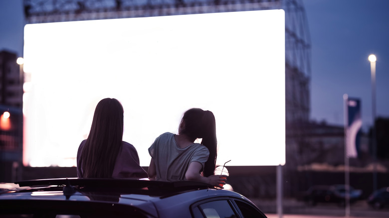 Two women sitting on their car at the drive-in