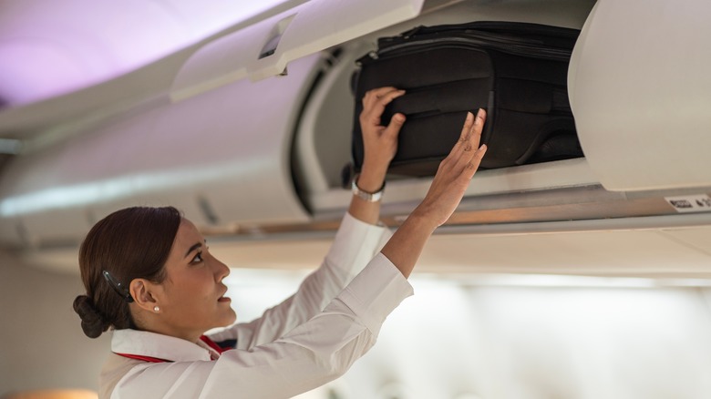 Flight attendant putting luggage in bin